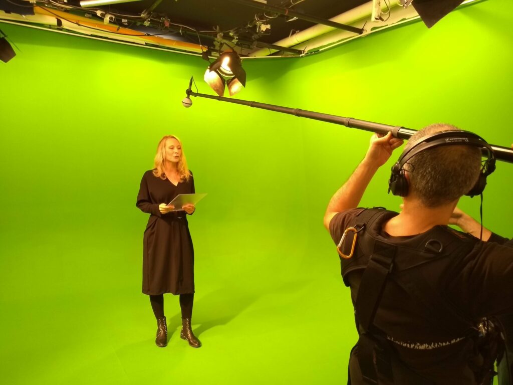 Présentatrice du faux JT Volvo France devant le fond vert du studio, avec la perche son au-dessus d’elle