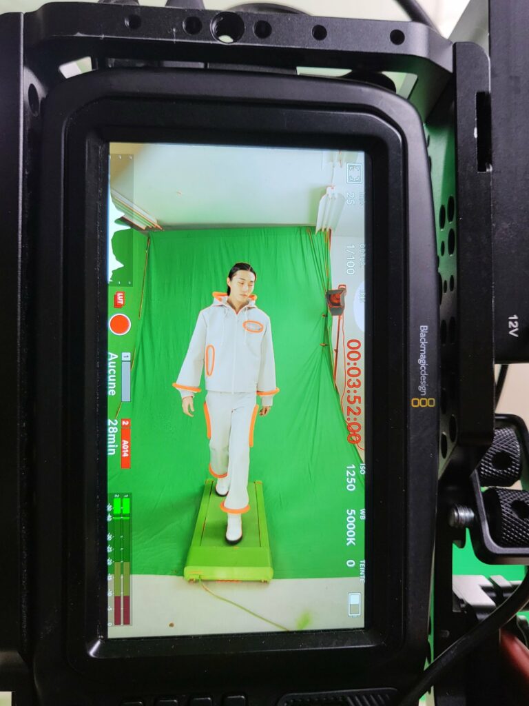 Moniteur de la caméra pendant le tournage pour Pierre Cardin : tenue blanche aux liserés orange filmée sur fond vert