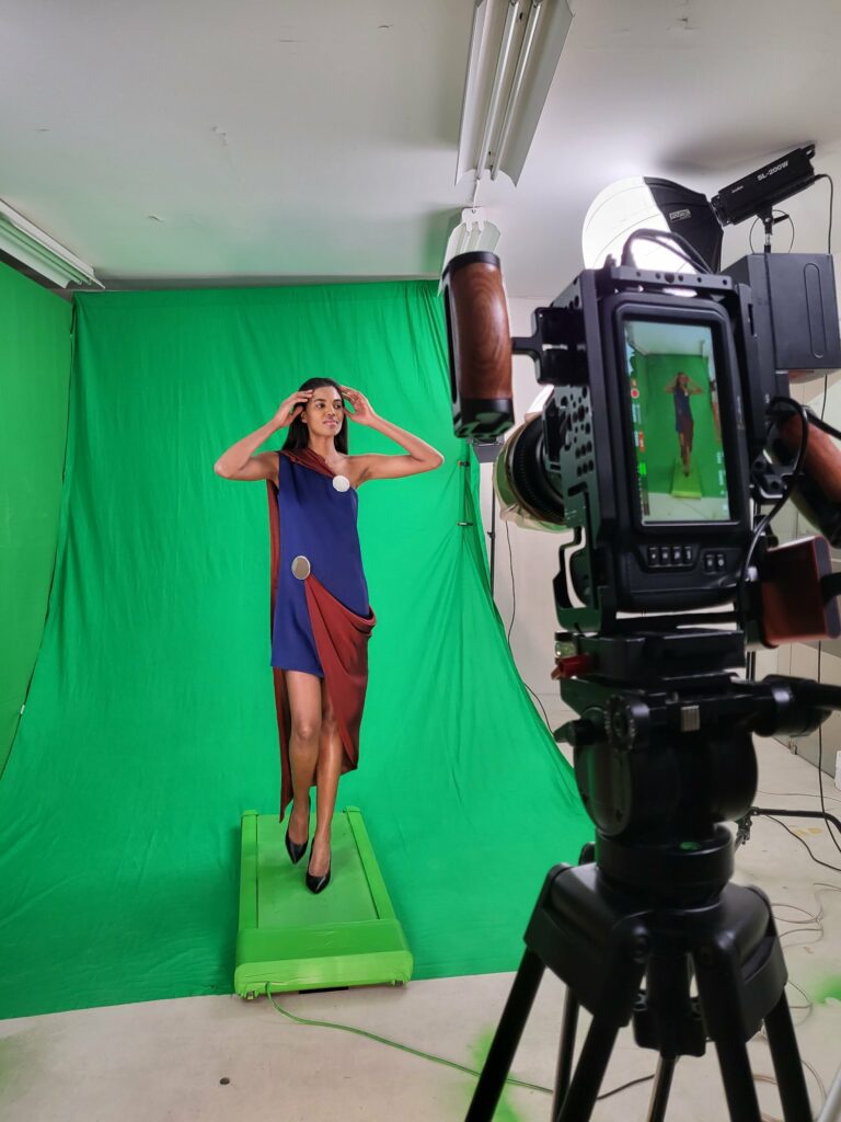 Mannequin en robe asymétrique bleue et bordeaux filmée sur fond vert, caméra sur pied au premier plan