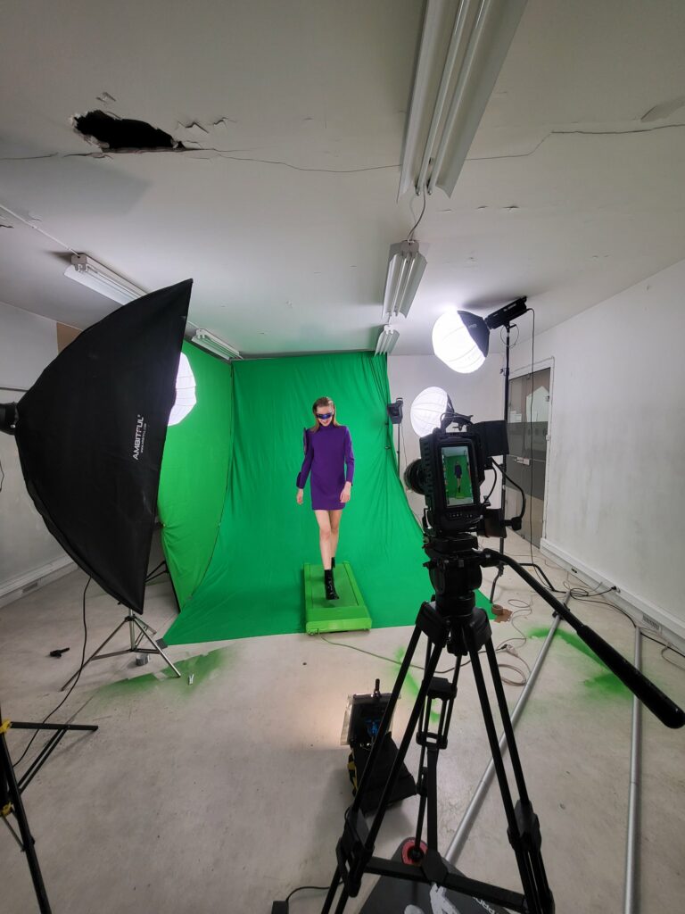 Mannequin en robe violette et lunettes bleues avançant sur le tapis roulant devant le fond vert