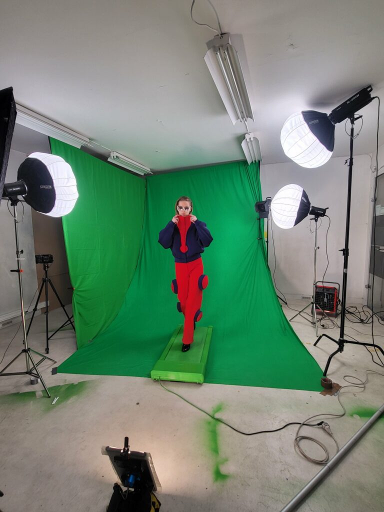 Mannequin en veste marine et pantalon rouge à pastilles, plan large du dispositif de lumière sur fond vert