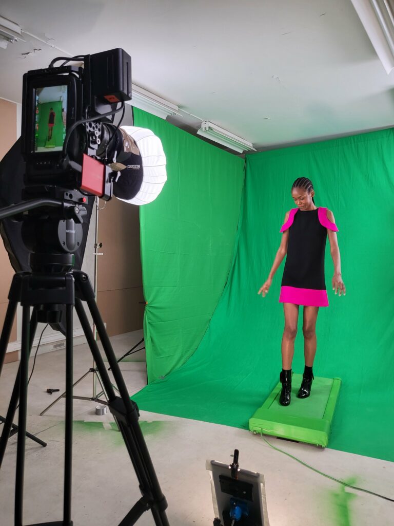 Mannequin en robe noire et rose fuchsia sur le tapis roulant, caméra et boule chinoise au premier plan